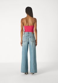 Ružový top bez ramienok a svetlomodré nohavice so širokými nohavicami, ktoré majú dve zadné vrecká a koženú nášivku na pásku. Hladká textúra.