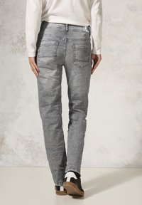 Jeans grigi sbiaditi con taglio dritto, caratterizzati da un classico design a cinque tasche e dettagli di cucitura sottili, indossati con sneakers nere.