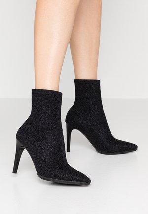 Bottines noires en tissu scintillant, avec un bout pointu et un haut talon stiletto. Texture lisse avec un ajustement confortable autour de la cheville.