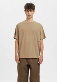 Pruun lühikeste varrukatega T-särk, lõdva lõikega, ümara kaelusega, valmistatud pehmest kangast; külje peal väike logodetail.