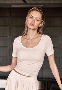 Haut beige clair à manches courtes et encolure dégagée, en matière douce, coupe ajustée, texture lisse, assorti à une jupe fluide et coordonnée.