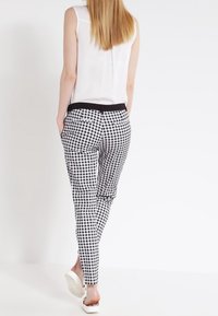 Pantalons à carreaux noir et blanc avec une coupe ajustée, ceinture élastique et poches latérales, associés à un haut sans manches blanc.