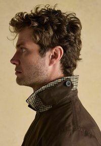 Brązkowa wodoodporna kurtka z kołnierzem w kratkę, z przyciskiem dekoracyjnym. Kołnierz jest podwinięty, aby ujawnić wewnętrzny wzór.