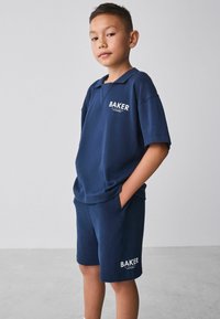 Marineblå polo shirt og shorts sæt lavet af blødt stof, med et hvidt "BAKER" print på begge dele. Løs pasform og korte ærmer.