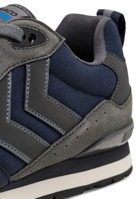 Sneaker med en marinblå mesh-överdel, grå suède-accenter och svart gummisula. Har en grå zigzag-design och grå snören, med synliga sömnadsdetaljer.