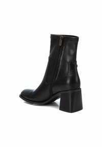 Bota de cuero negro hasta el tobillo con punta redondeada, cremallera lateral y un tacón bloque texturizado. Acabado suave con acentos mínimos de hardware.