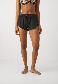Schwarze sportliche Shorts mit einem Kordelzugbund, seitlichen Schlitzen und einer glatten Textur, kombiniert mit einem blümchenmusternden Bikinioberteil.