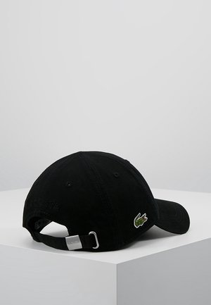 Casquette de baseball noire Lacoste avec sangle réglable et boucle métallique, arborant un logo crocodile vert brodé sur le côté, présentée sur une surface blanche.