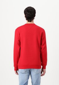 Rød sweatshirt med lange ærmer, rund halsudskæringer, ribbede manchetter og kant. Har en let V-søm detalje på ryggen. Båret med lyseblå jeans.