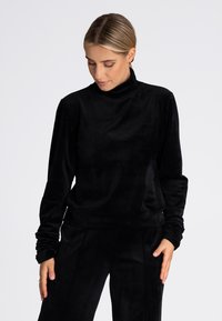 Czarna aksamitna bluza z golfem, długimi rękawami i zwężanymi mankietami, charakteryzująca się gładką, miękką teksturą oraz luźnym fasonem.