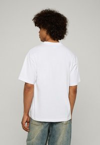 Balta kokvilnas T-kreklu ar brīvu piegriezumu, apaļu kaklu un īsām piedurknēm. Gluda tekstūra ar minimālu šuvju skaitu un bez redzamām grafikām.