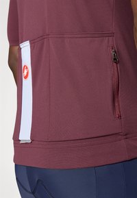 T-shirt de sport bordeaux à manches courtes, en tissu évacuant l'humidité, avec une poche zippée à l'arrière et des accents bleu clair contrastants. Logo affiché sur le côté.