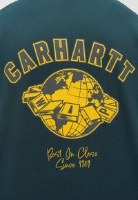 Dark green sweatshirt featuring a yellow globe graphic surrounded by books. "CARHARTT" and "Best In Class Since 1989" text included.