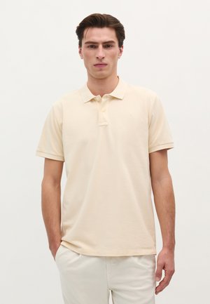 Hellbeige Poloshirt aus atmungsaktiver Baumwolle. Verfügt über eine Knopfleiste mit drei Knöpfen, kurze Ärmel und ein dezentes, auf die Brust gesticktes Logo.