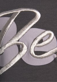 Le tissu gris foncé présente de grandes formes circulaires violet clair et des lettres brodées en argent métallique, offrant une texture lisse.