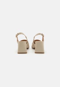 Beige høyhælte sandaler med firkantet blokkhel og ankelrem. Glatt lærmateriale med brun såle og justerbar metallspenne.