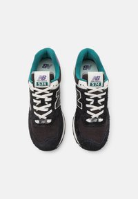 Baskets New Balance 574 en noir et blanc avec des accents turquoise, composées de mesh et de daim, lacets plats et col rembourré.