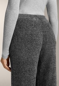Šedé rebrované pletené nohavice s textúrovanou tkaninou, so širokým elastickým pásom a voľným strihom, v kombinácii s priliehavým šedým topom s dlhými rukávmi.