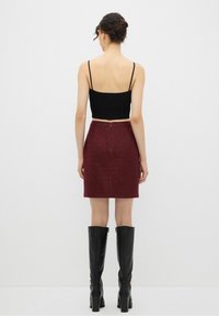 Černý žebrovaný crop top, vínová strukturovaná mini sukně se zipem vzadu a černé kožené vysoké boty s blokovými podpatky.