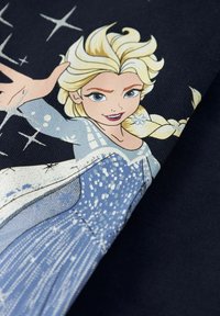 Blondínka s vrkočom a modrými očami v trblietavých svetlomodrých šatách, ktorá predlžuje ruku s okolo snehovými vločkami.