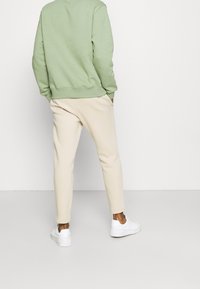 Mintgrön sweatshirt med ribbade muddar och nederkant, i kombination med beiga byxor med smal passform och vita sneakers. Slät tygtextur genomgående.