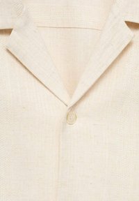 Beige Leinenblazer mit Reverskragen und einem einzelnen cremefarbenen Knopfverschluss am Hals, mit einer strukturierten Stoffoberfläche und dezentem Webmuster.