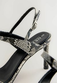 Sandalo con tacco alto in pelle di serpente nera e grigia, caratterizzato da una punta affusolata, cinturino alla caviglia con fibbia argentata e interno liscio.