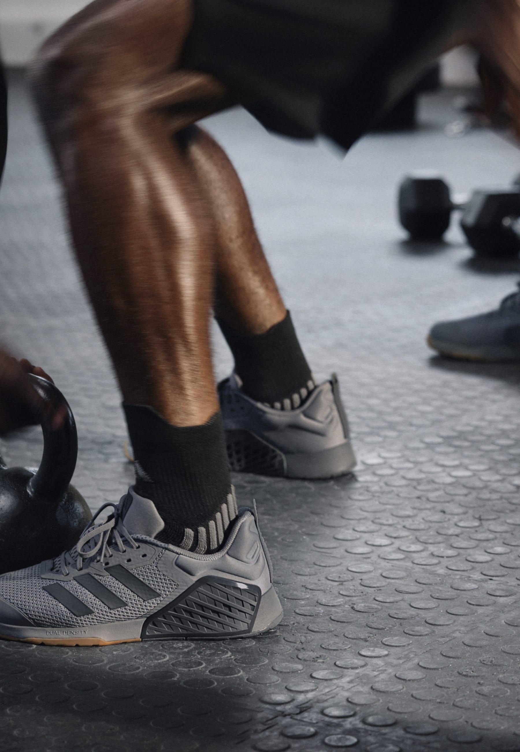 Baskets de sport grises avec une tige texturée, présentant un design en maille, une semelle en caoutchouc et des détails en noir, positionnées près d'un kettlebell.