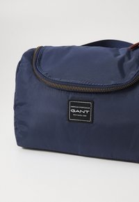 Marineblå nylon duffelbag med glidelås, med en teksturert overflate og en svart etikett med hvit tekst.