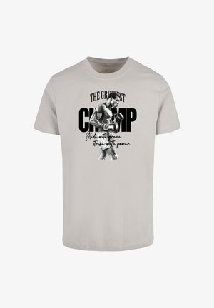 Gaišs pelēks kokvilnas T-krekls ar melnbaltu boksera grafiku, ar tekstu "LIELĀKAIS ČEMPIONS" un citātu zem tā.