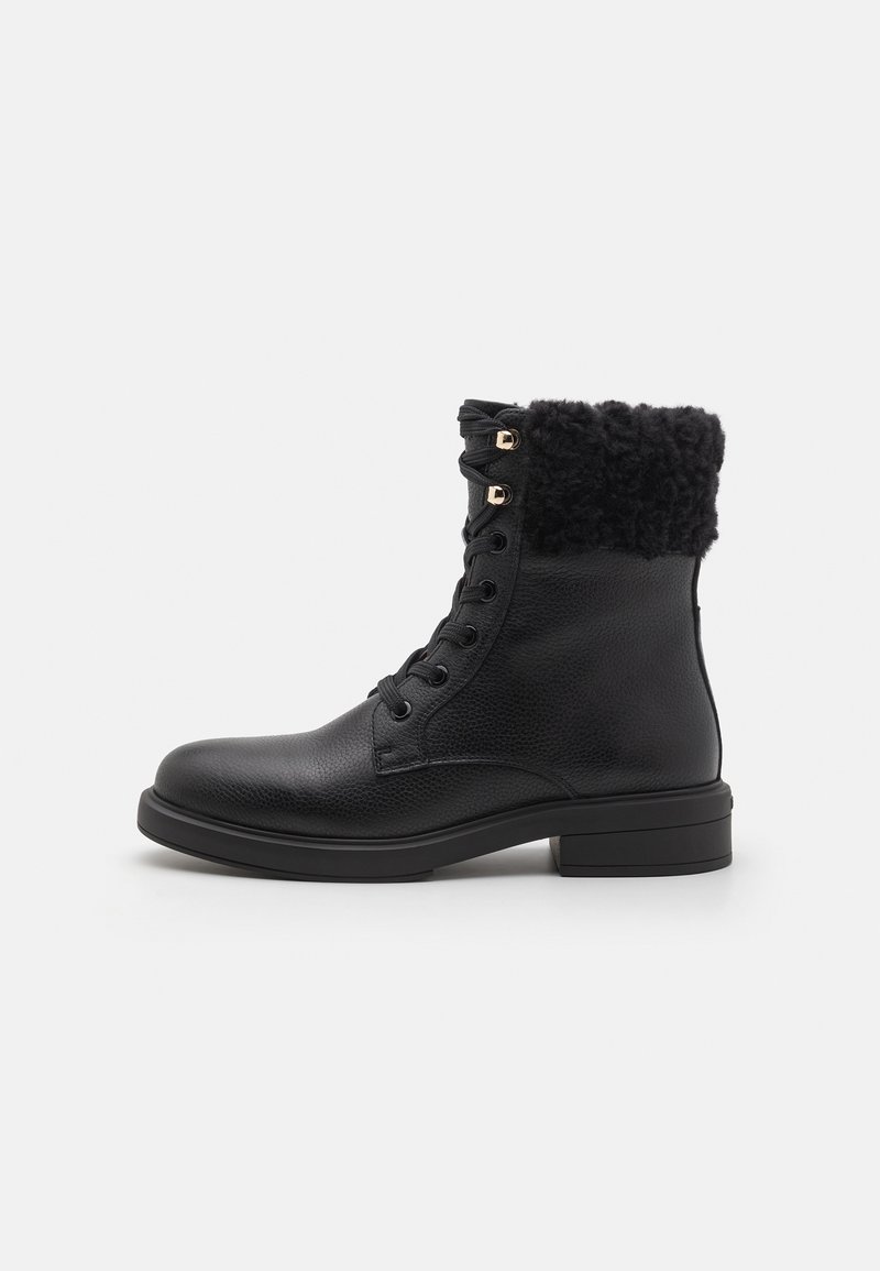 Bottine noire en cuir avec lacets à l'avant, œillets dorés, semelle épaisse et col en fausse fourrure noire, vue de côté sur fond blanc.