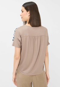 Kortærmet top i blødt taupe-stof med en samlet detalje bagpå; farveblokeret blomster mønster på ærmerne tilføjer visuel interesse.