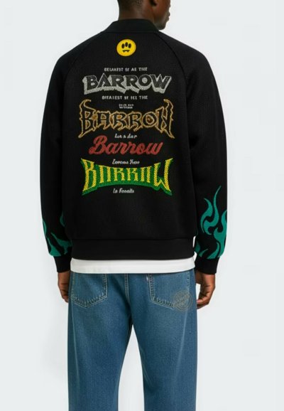 Mężczyzna w czarnej kurtce z kolorowymi napisami "Barrow" na plecach i turkusowymi wzorami płomieni na rękawach, w połączeniu z niebieskimi dżinsami.
