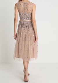 Vestido rosa empolvado con parte superior transparente, adornado con lentejuelas florales multicolores; falda hasta la rodilla con tela fruncida, cierre de cremallera en la parte posterior.