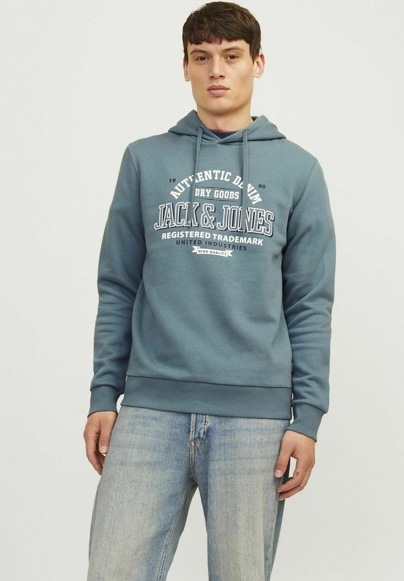 Hættebluse i teal bomuldsblanding med et grafisk logo fortil, ribbede manchetter og kant, samt en afslappet pasform. Bæres sammen med lyse denimjeans.