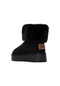 Botín negro con puño de piel sintética, parte superior de ante, suela plana de goma y un parche rectangular marrón con logo en el lateral.