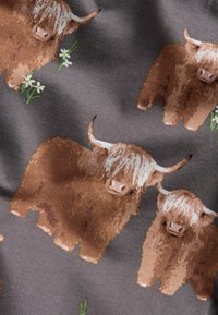 Stof med et gentaget mønster af brune Highland-kvæg med lyst pels og horn, sat mod en grå baggrund med grøn græs og margueritter.