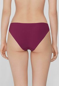 Bikini-Unterteile in einem tiefen Burgunderrot, aus glattem Stoff gefertigt. Sie haben einen niedrigen Schnitt mit nahtlosem Finish und minimalistischem Design.