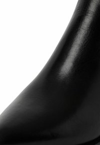 Zapato de tacón alto de cuero negro con una superficie pulida y elegante. Presenta una punta afilada y una silueta suave y curva.