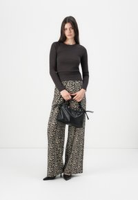 Braun enganliegendes Langarmoberteil kombiniert mit weiten Leopardenmuster-Hosen. Hält eine schwarze strukturierte Handtasche mit Kordelzugverschluss. Schwarze spitze Schuhe.