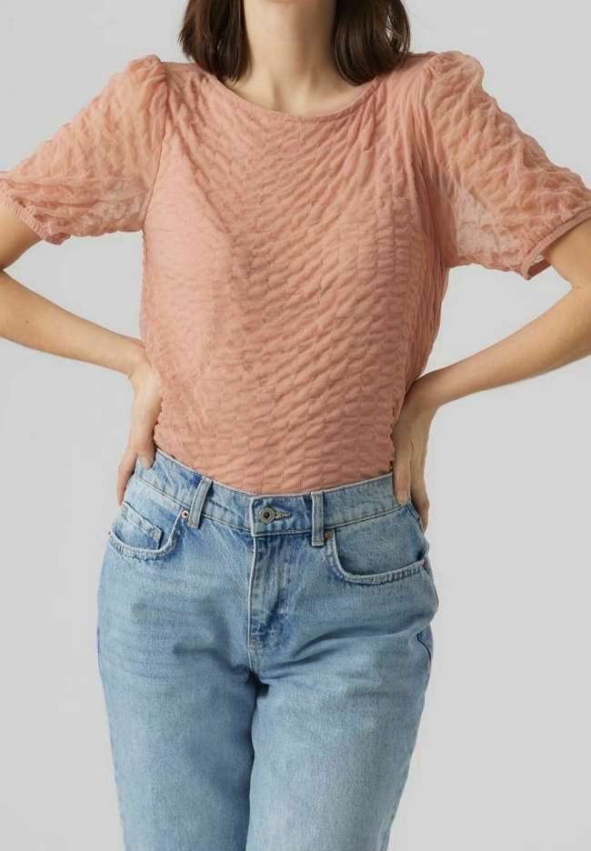 Texturierte, pfirsichfarbene Bluse mit Puffärmeln, kombiniert mit hellblauen, klassischen Denim-Jeans mit vorderen Taschen und Knopfverschluss.