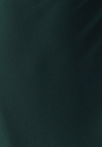 Tmavozelená textúrovaná látka s jemnými záhybmi a tieňmi, vytvárajúca mäkký a hladký vzhľad povrchu.