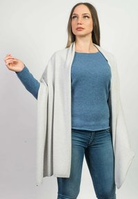 Grå åben cardigan hænger over en blå sweater, begge lavet af blødt stof. Blå jeans fuldender outfittet og viser et afslappet men lagdelt udseende.