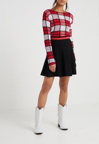 Red and white checkered cropped sweater, black flared skirt, and white cowboy boots. Sweater has long sleeves and a ribbed texture.