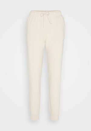 Béžové jogger nohavice vyrobené z mäkkej tkaniny, s elastickým pásom na šnúrku, zúženými nohavicami a malým logom v blízkosti bokov.