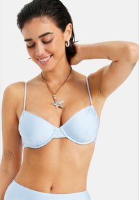 Lyseblå bikini topp med tynne justerbare stropper, myk tekstur, undertråd støtte og sømløst design, vist med en sjøstjernemedaljong. 