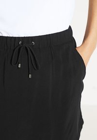 Černé šortky s elastickým pasem a stahovací šňůrkou. Mají boční kapsy a hladkou, lehkou texturu látky.