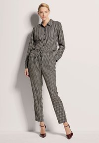 Zwart-wit gestreepte jumpsuit met lange mouwen, knoopsluiting, en elastische taille, gecombineerd met puntige paarse hakken.