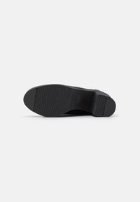 Suela de zapato negra con un patrón texturado y acanalado. Forma ligeramente redondeada y material duradero. Tacón de perfil bajo para estabilidad.
