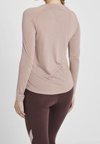 Långärmad, åtsittande topp i mjuk mauve-tyg med rundad halsringning och raglanärmar, kombinerad med mörk vinröda leggings.
